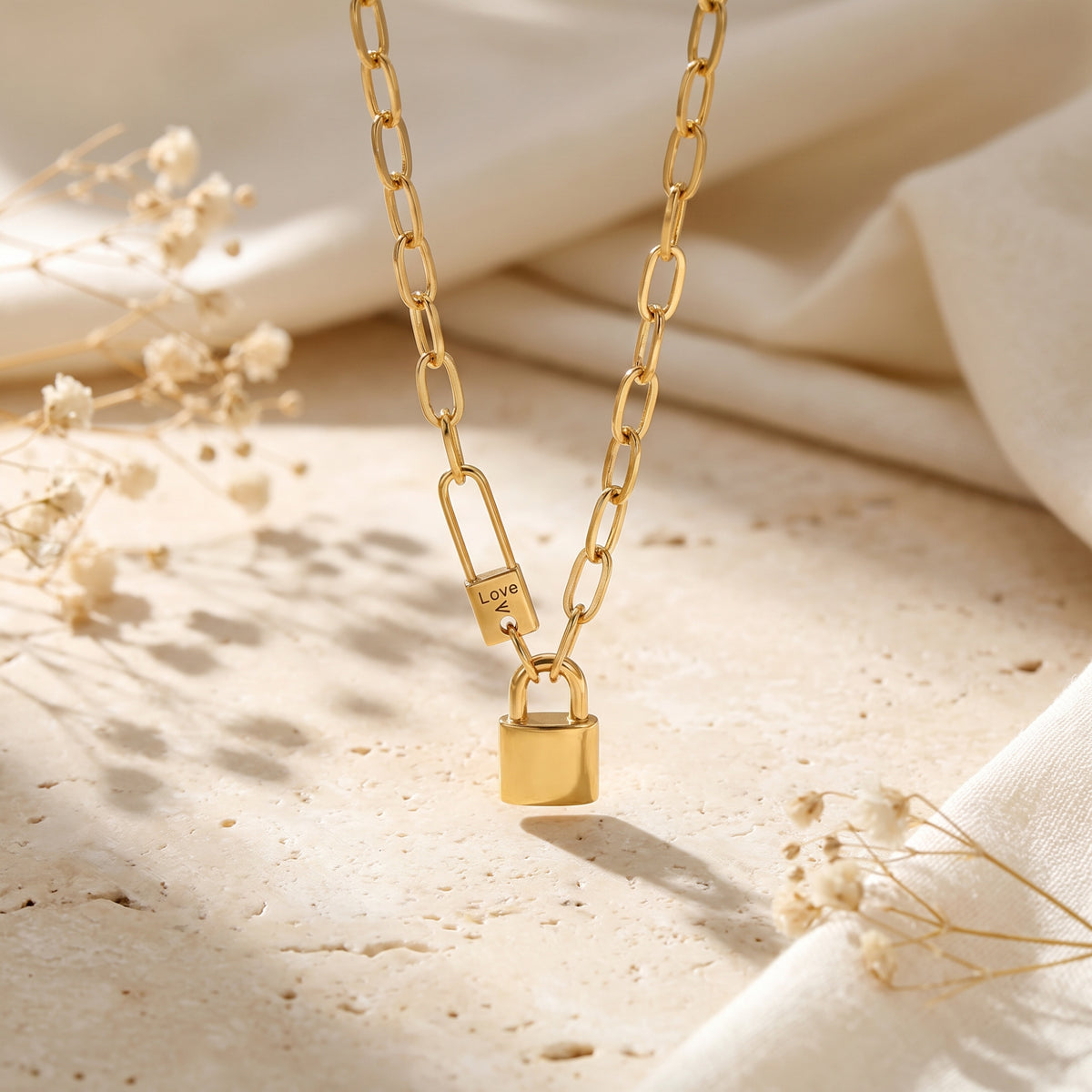 Gold-tone paperclip chain necklace with a lock charm suspended over a textured background.