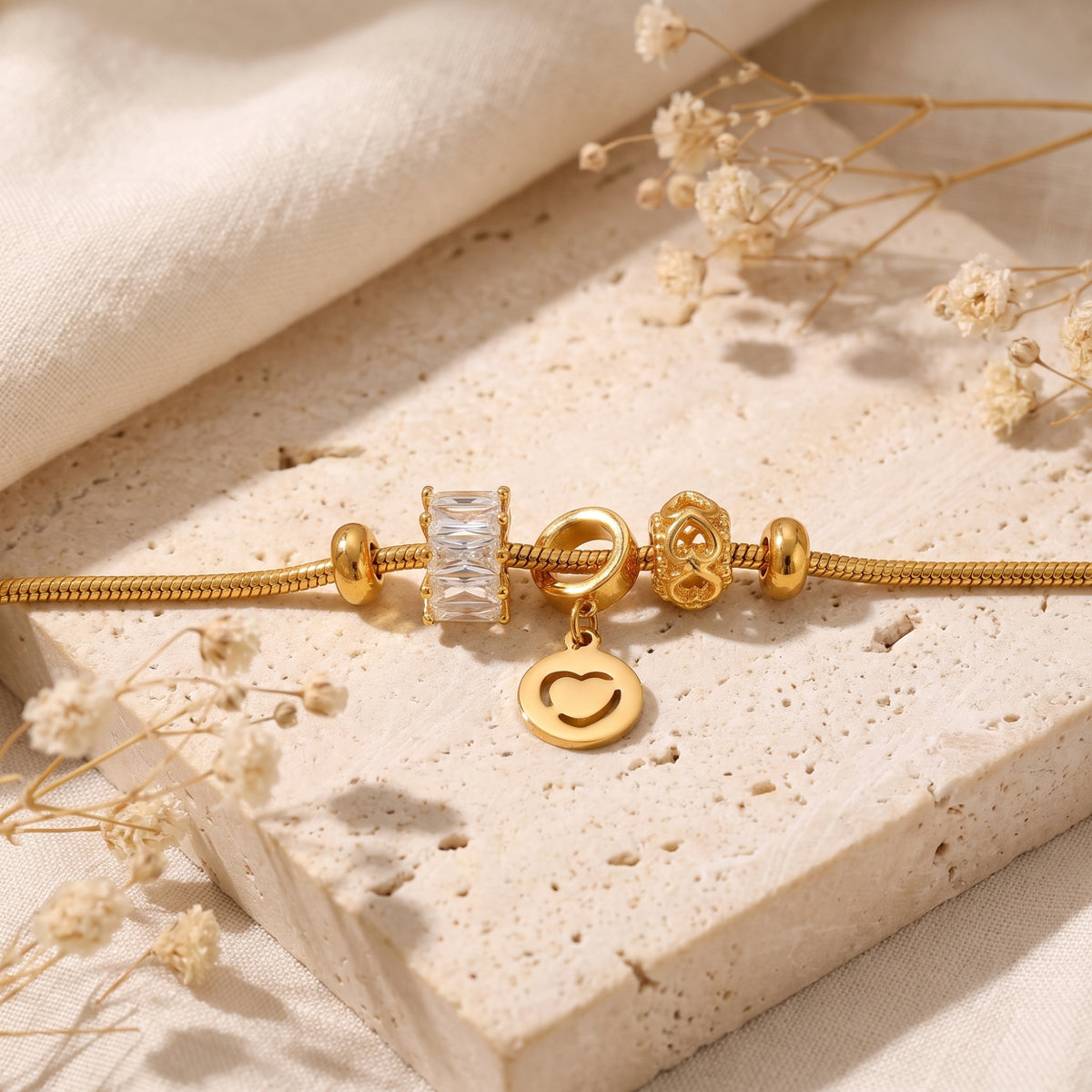 Close-up of the gold-tone bracelet charms, including the heart pendant and crystal accent, resting on stone.