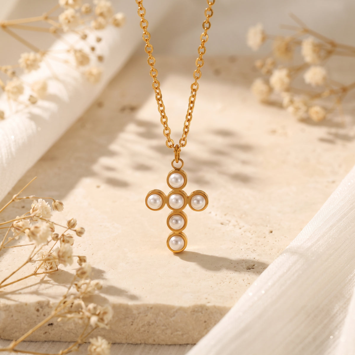 Front view of the gold cross necklace with six round white simulated pearls hanging over a stone display base.