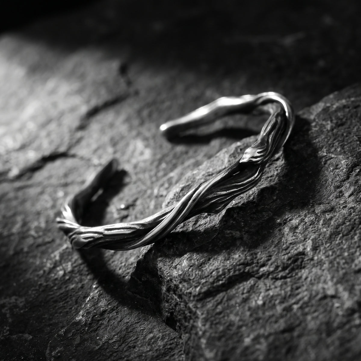 Angled close-up of the silver twisted vine cuff bracelet on textured dark stone.
