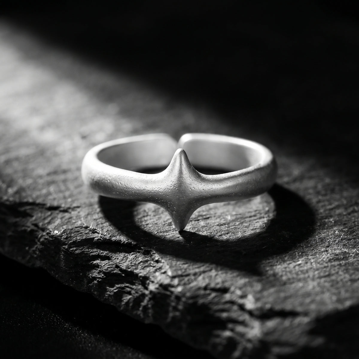 Close-up of the matte silver open band ring lying on slate, with its four-point star motif facing the camera.