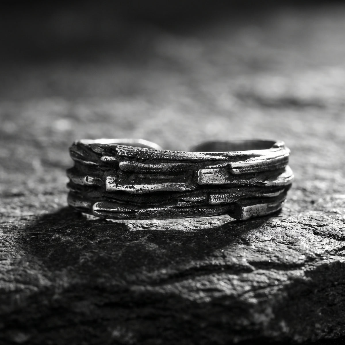 Close-up of the textured oxidized silver open band ring resting horizontally on a dark rock.