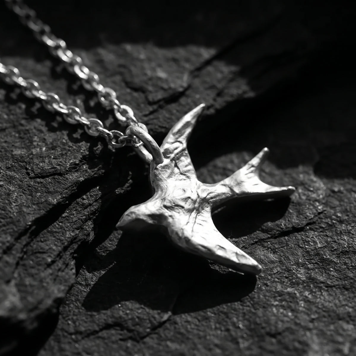 Angled close-up of the textured silver swallow pendant and chain on dark slate.