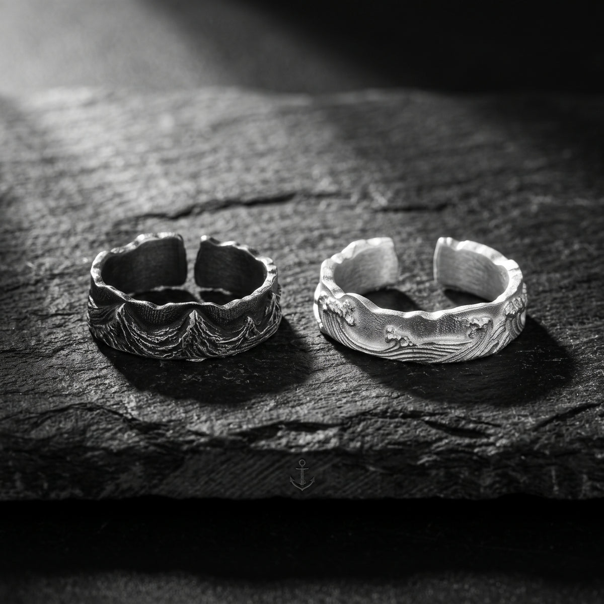Front view of dark-toned and bright silver wave open-band rings standing side by side on slate.