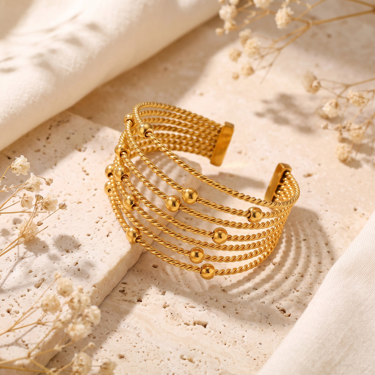 Angled view of the open gold-tone multi-strand twisted cable cuff bracelet on a textured stone surface.
