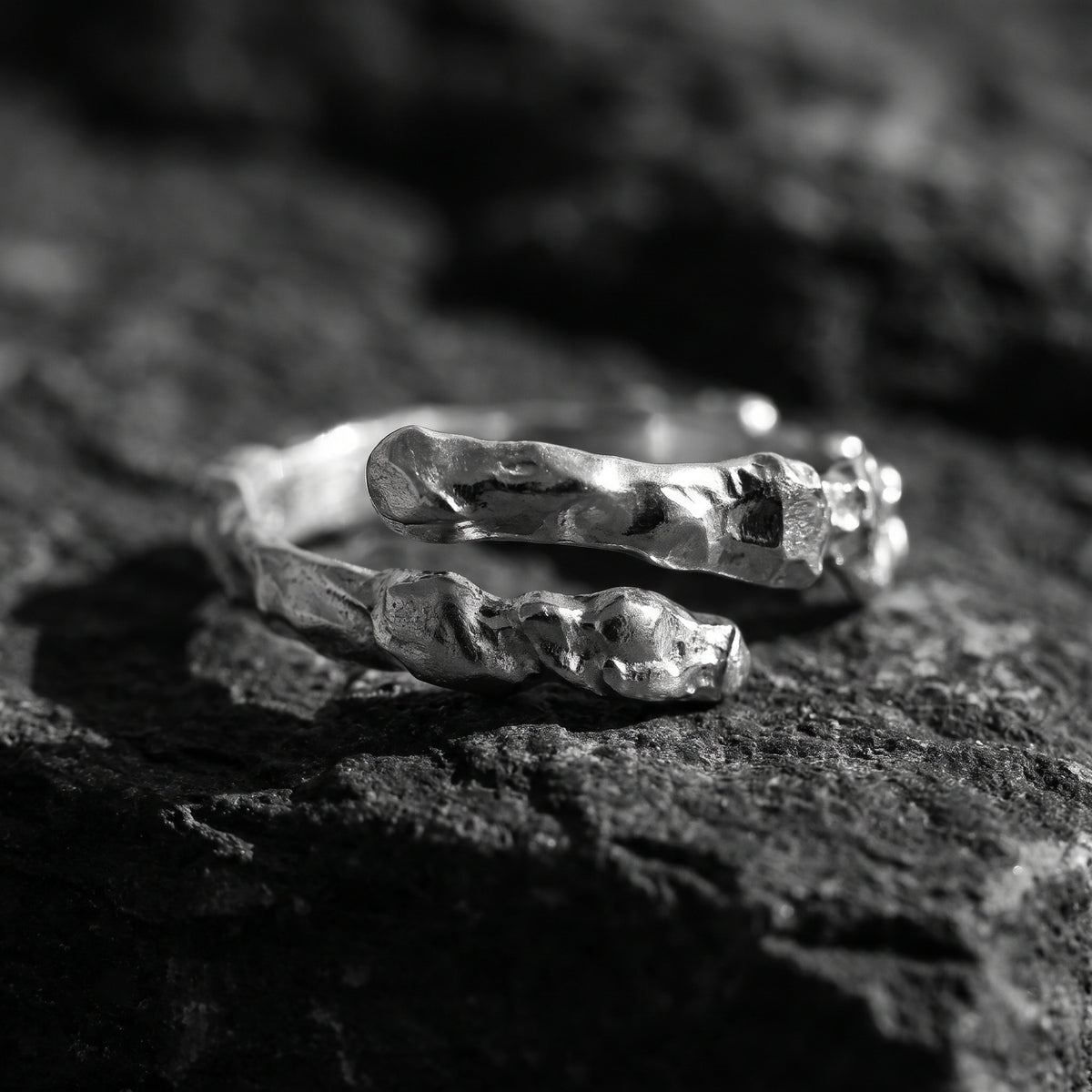 Close-up of the textured ends of the silver molten open bypass ring lying on black rock.