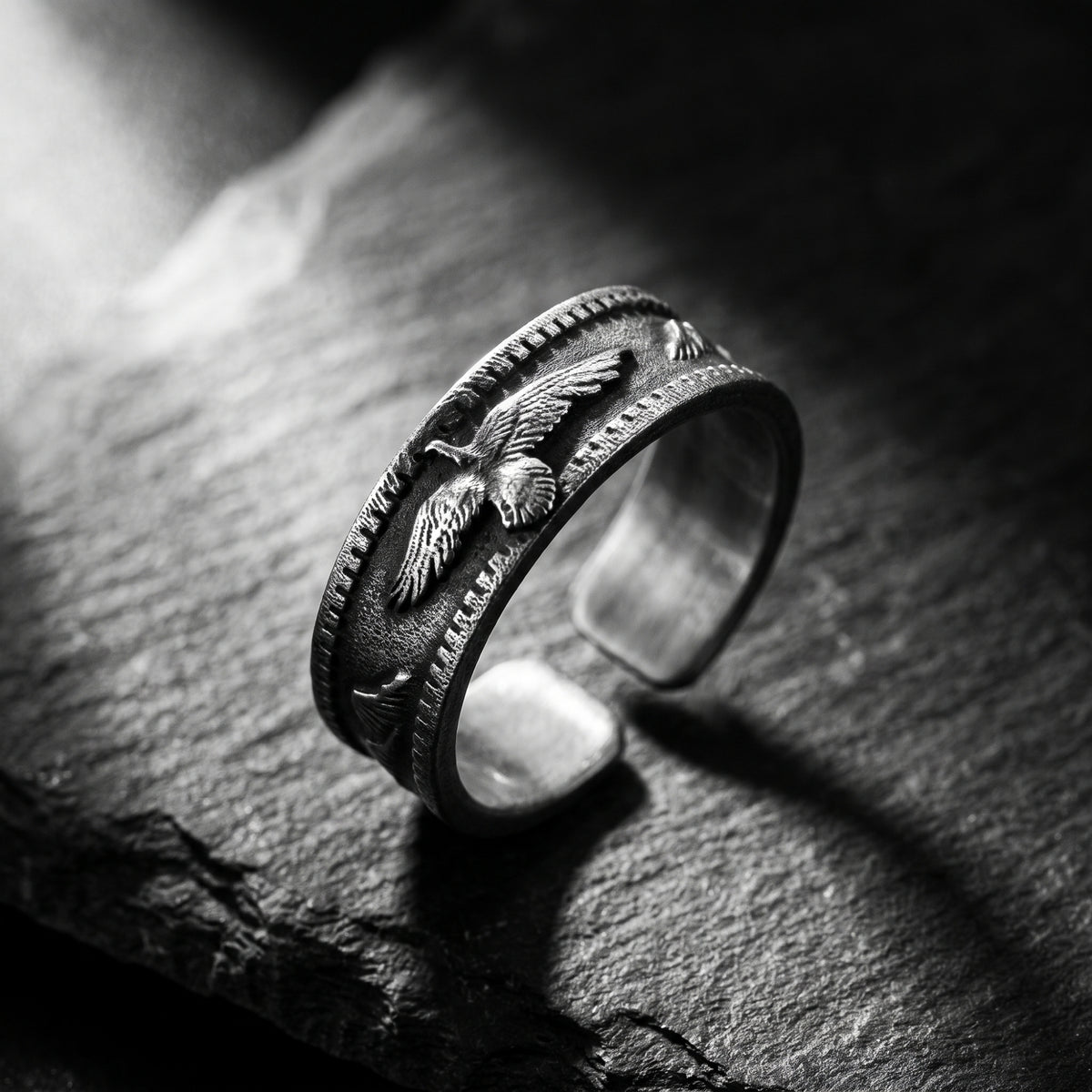 Angled view of the silver open-band ring showing its eagle relief and open gap on a textured stone surface.