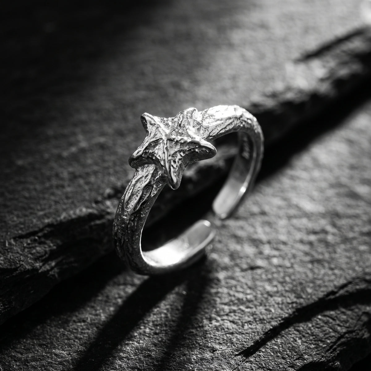 Angled view of a silver star ring on dark rock, showing its open band.
