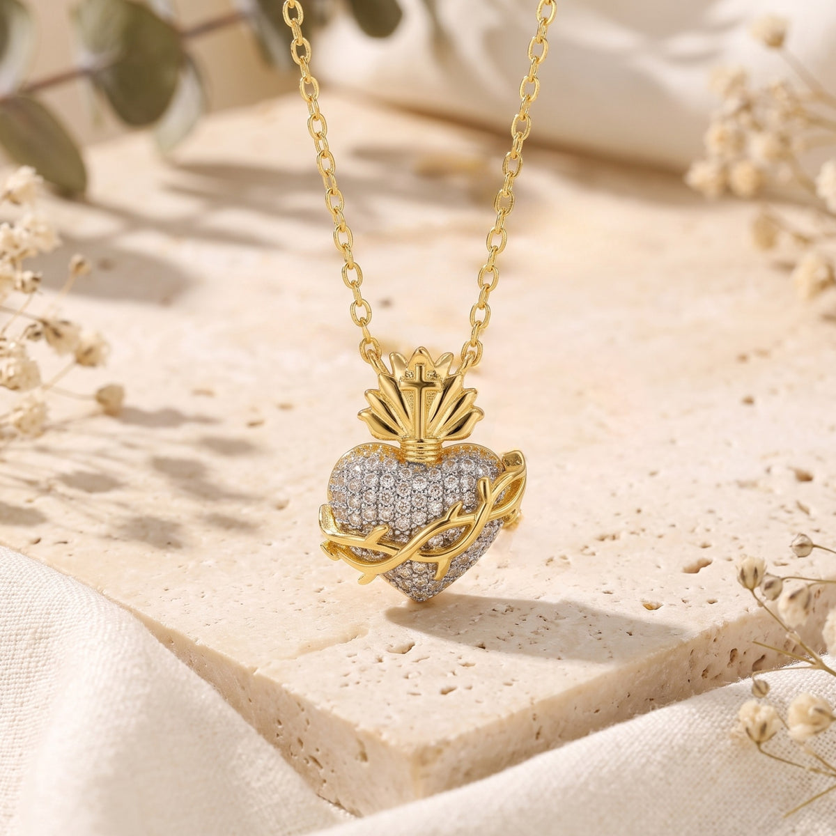 Upright front view of the gold-tone sacred heart pendant with cubic zirconia pavé, hanging above a pale stone surface.