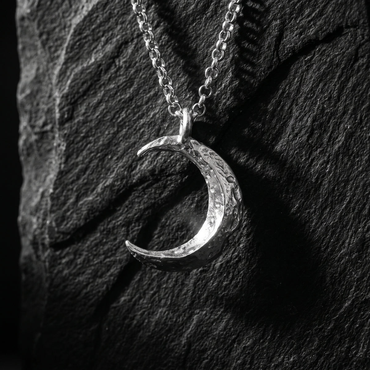 Silver textured crescent moon pendant hanging vertically against a dark stone surface.