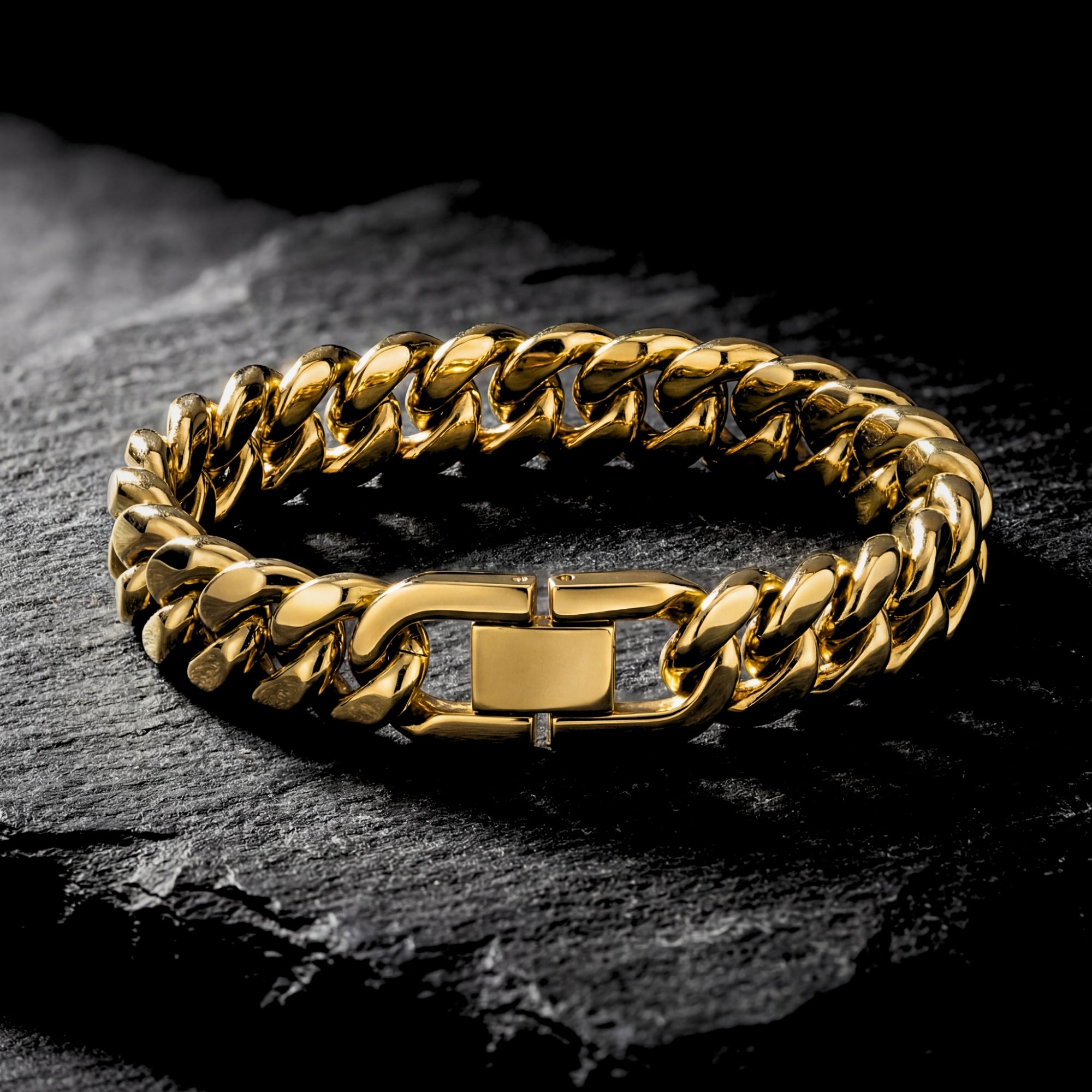 Detailed view of the clasp on a gold stainless steel Cuban link bracelet against a dark stone background.
