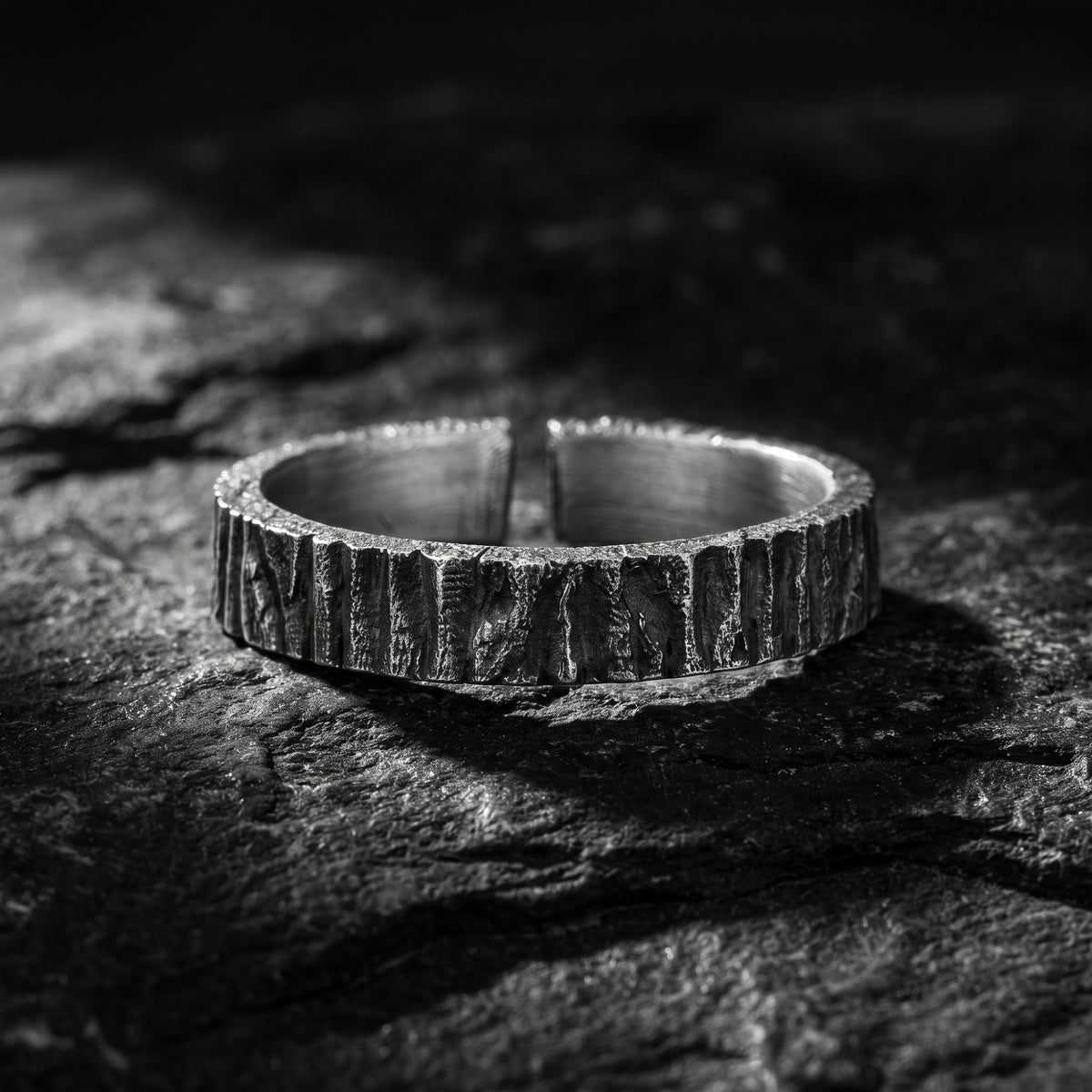 Front view of the textured silver open band ring resting on rough dark rock, with the gap visible at the top.