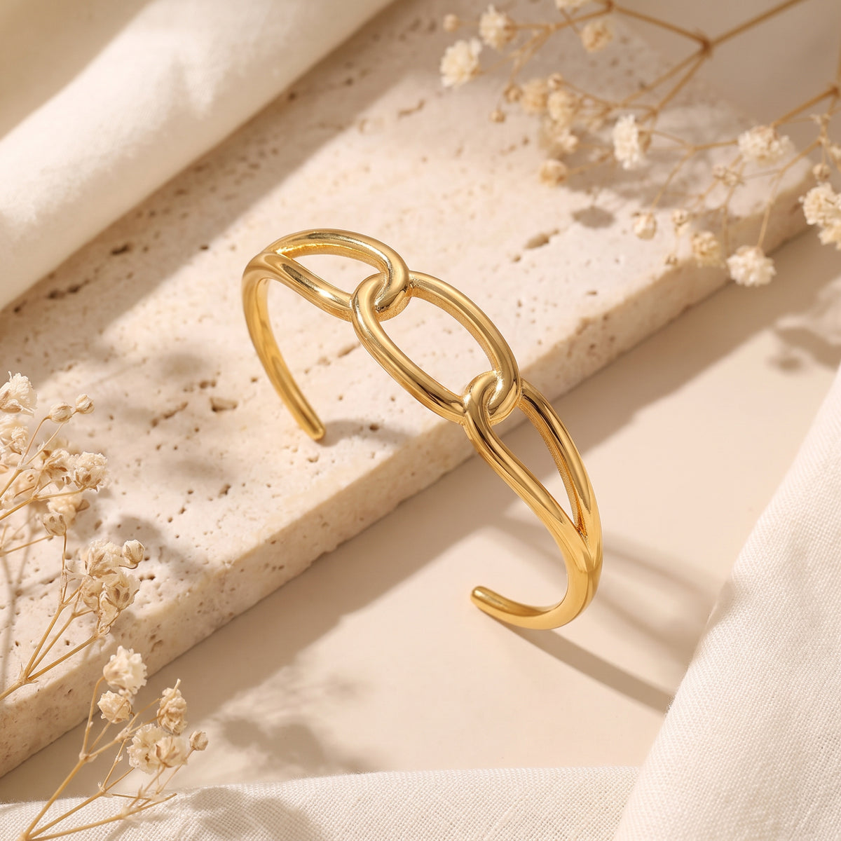 Angled view of the gold-tone open cuff bracelet with linked oval loops on a porous stone slab.