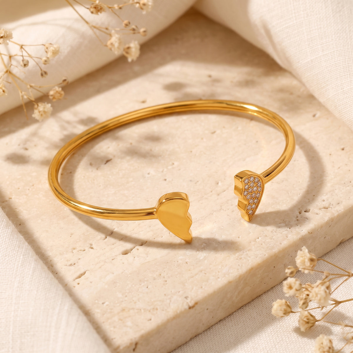 Angled view of the gold-tone open cuff bracelet displaying one smooth heart half and one crystal-paved heart half.