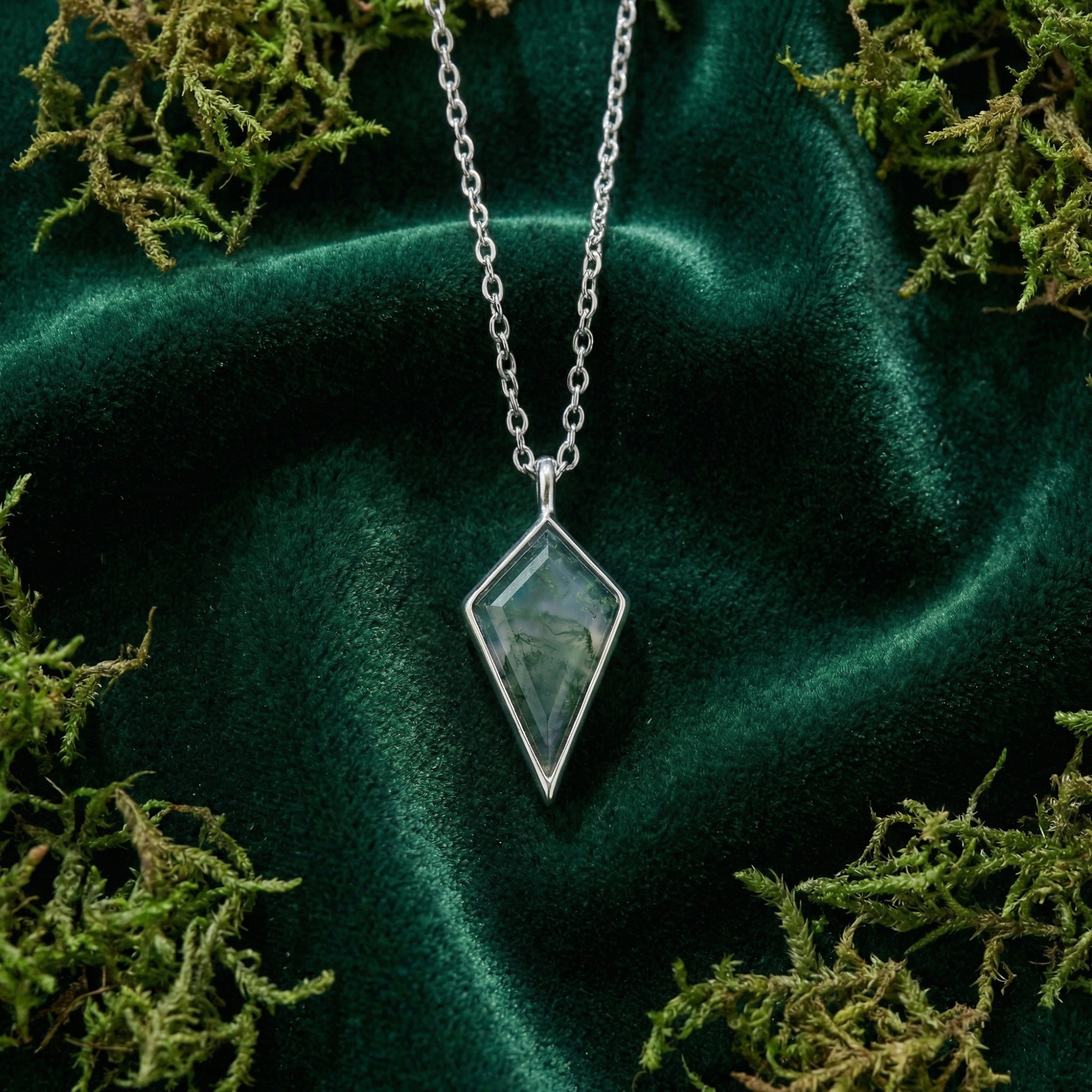 Close-up of a kite cut moss agate pendant in S925 sterling silver, showing unique green inclusions on velvet.