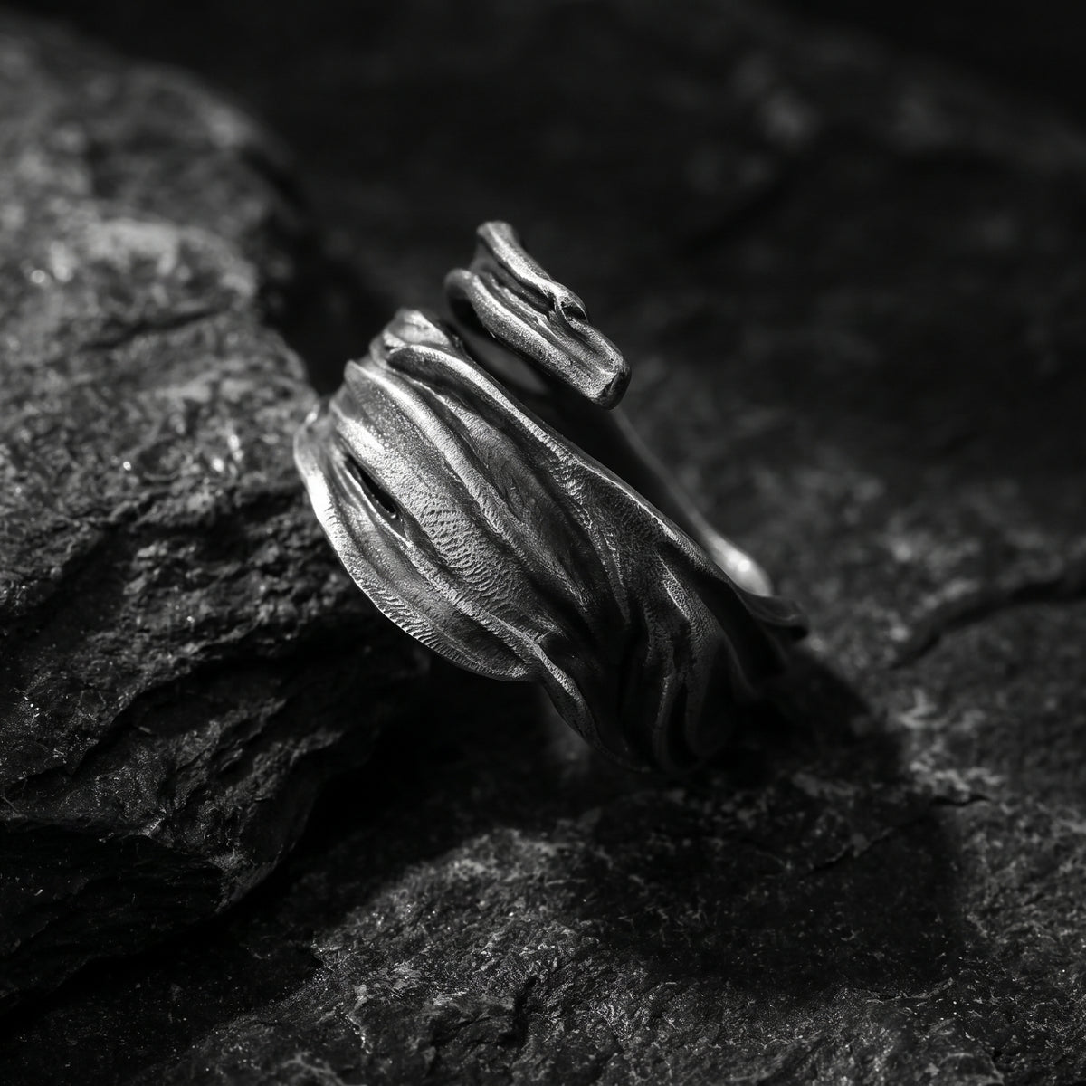 Close-up of the textured silver open ring displayed upright at an angle on dark rock.