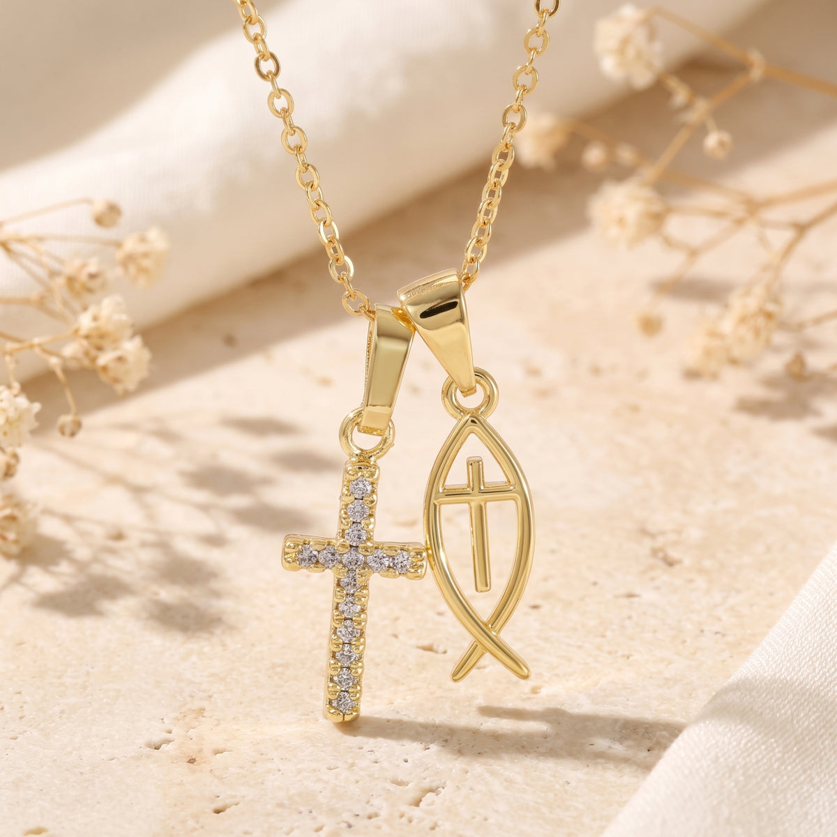 Detailed view of the cubic zirconia cross and Ichthys fish pendants on a gold-tone chain.