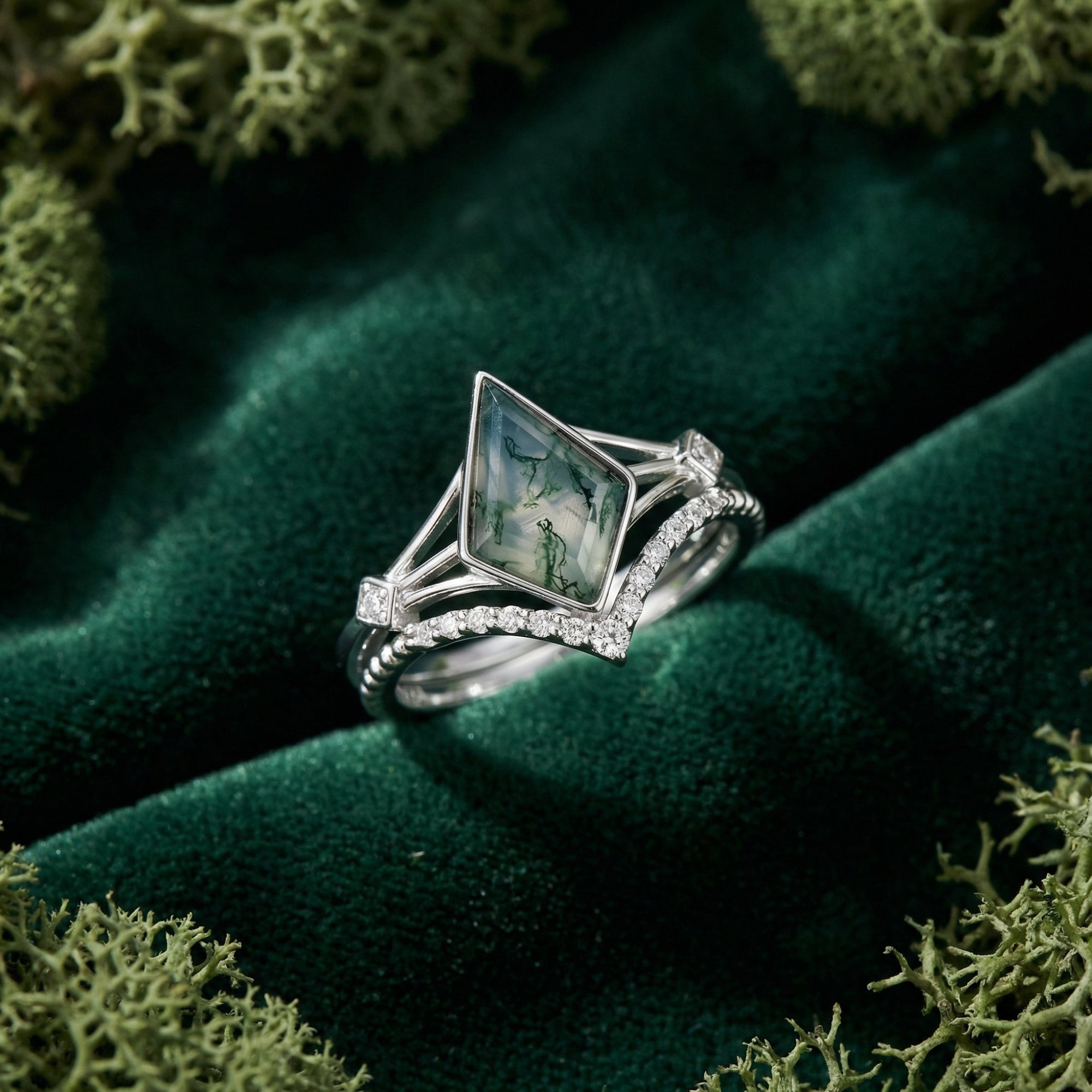 Angled view of a kite cut moss agate and S925 sterling silver solitaire ring set resting on green velvet with moss.