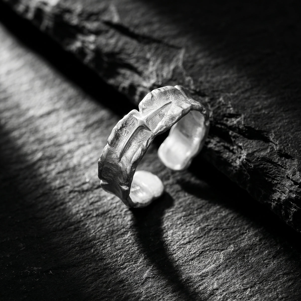 Angled view of a textured silver open-band ring on dark slate, showing its opening and raised starburst motif.