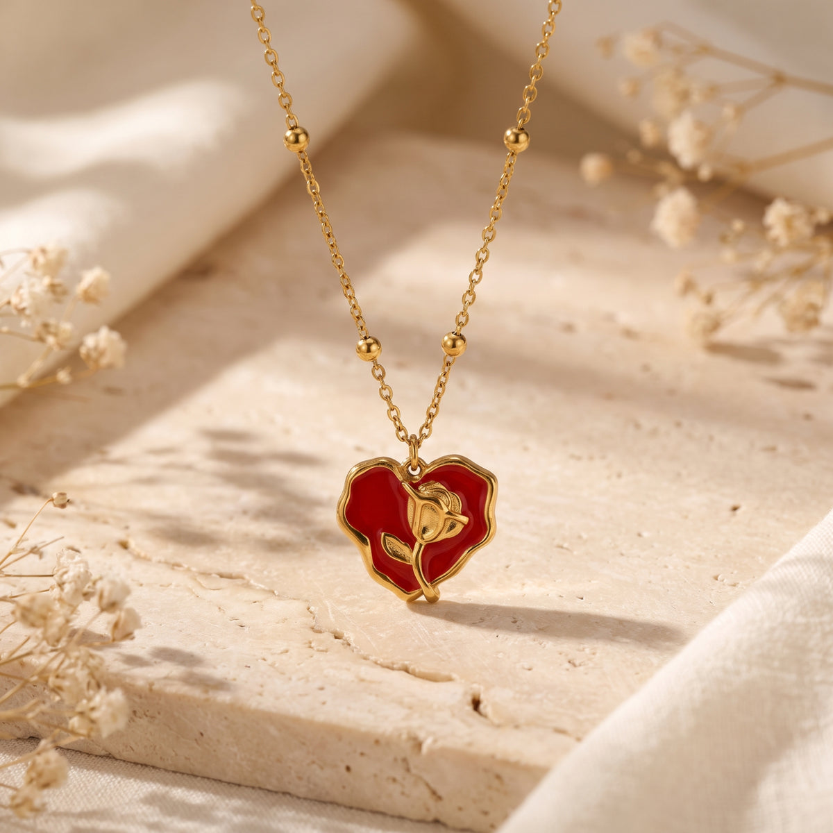 Close-up of the red enamel heart pendant with a raised gold-tone rose, suspended from a beaded station chain.