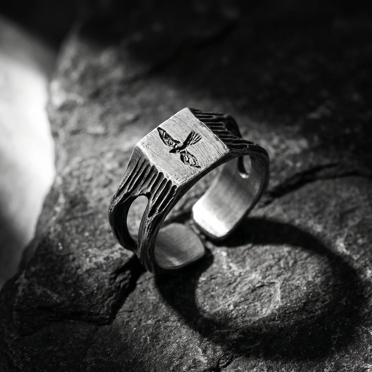 Angled close-up of the silver signet ring showing its carved falcon motif and open band on stone.