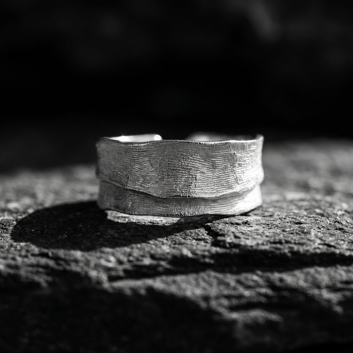 Low front view of the textured silver open-band ring resting on dark rock