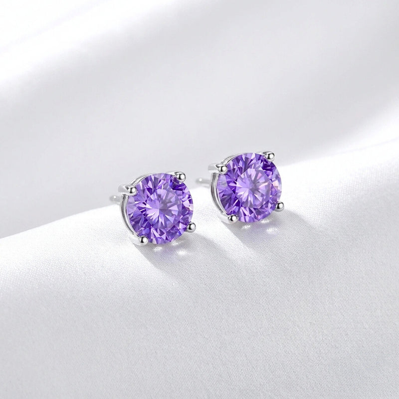 Side view of round cut simulated amethyst sterling silver stud earrings resting on white silk fabric.