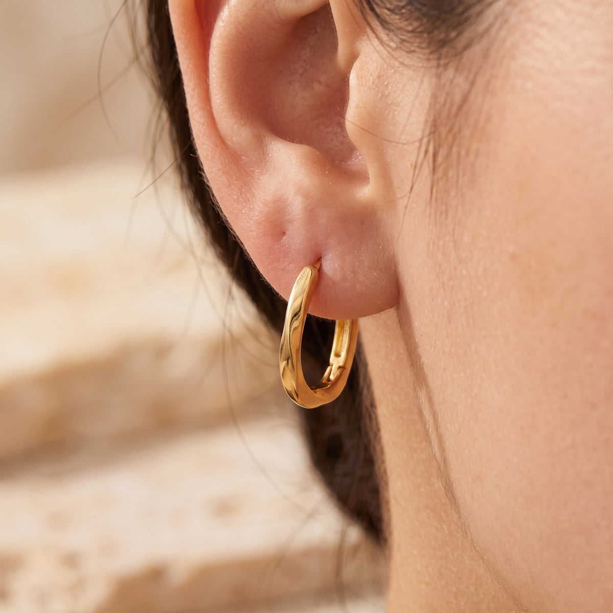 Close-up back angle of a gold-toned twisted hoop earring worn on an ear, with its latch clasp visible.