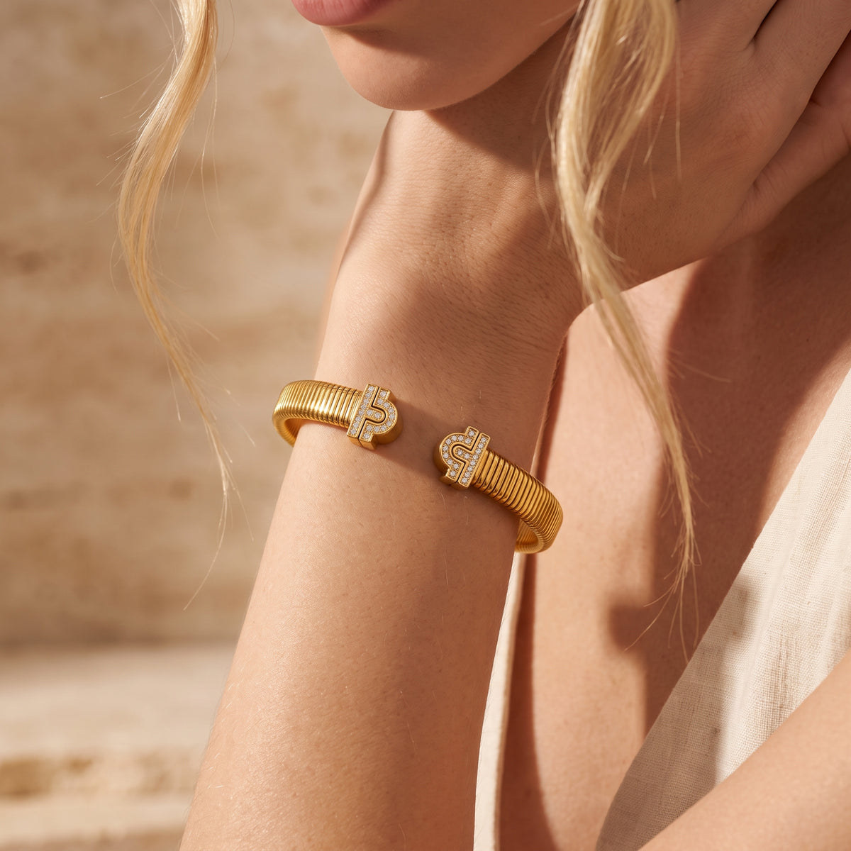 Close view of a gold-finish ribbed open cuff bracelet with cubic zirconia ends worn on a wrist.