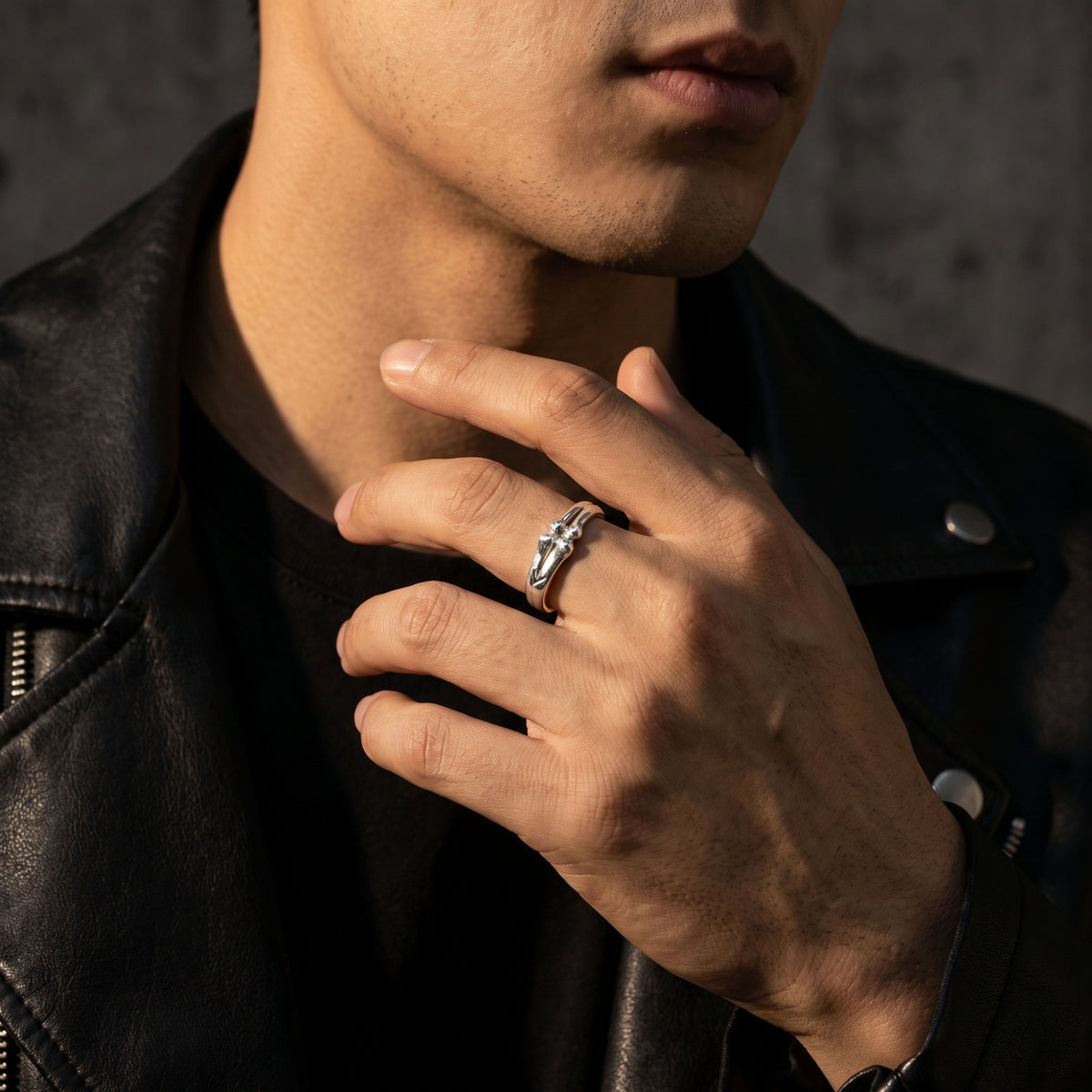 Man in a black leather jacket wearing the silver bone-motif open band ring on his middle finger.