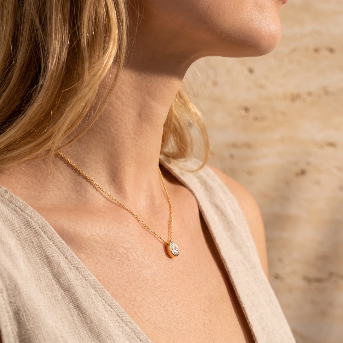 Side-profile view of a model wearing the gold-tone teardrop bezel pendant necklace.