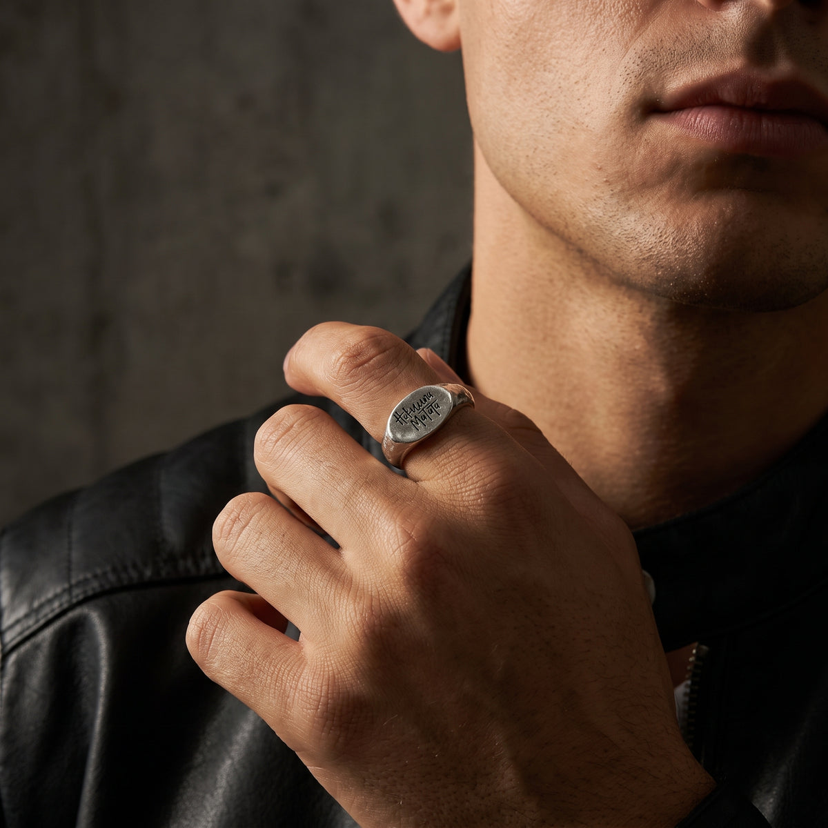 Close-up of a hand wearing the silver Hakuna Matata signet ring against a black leather jacket.