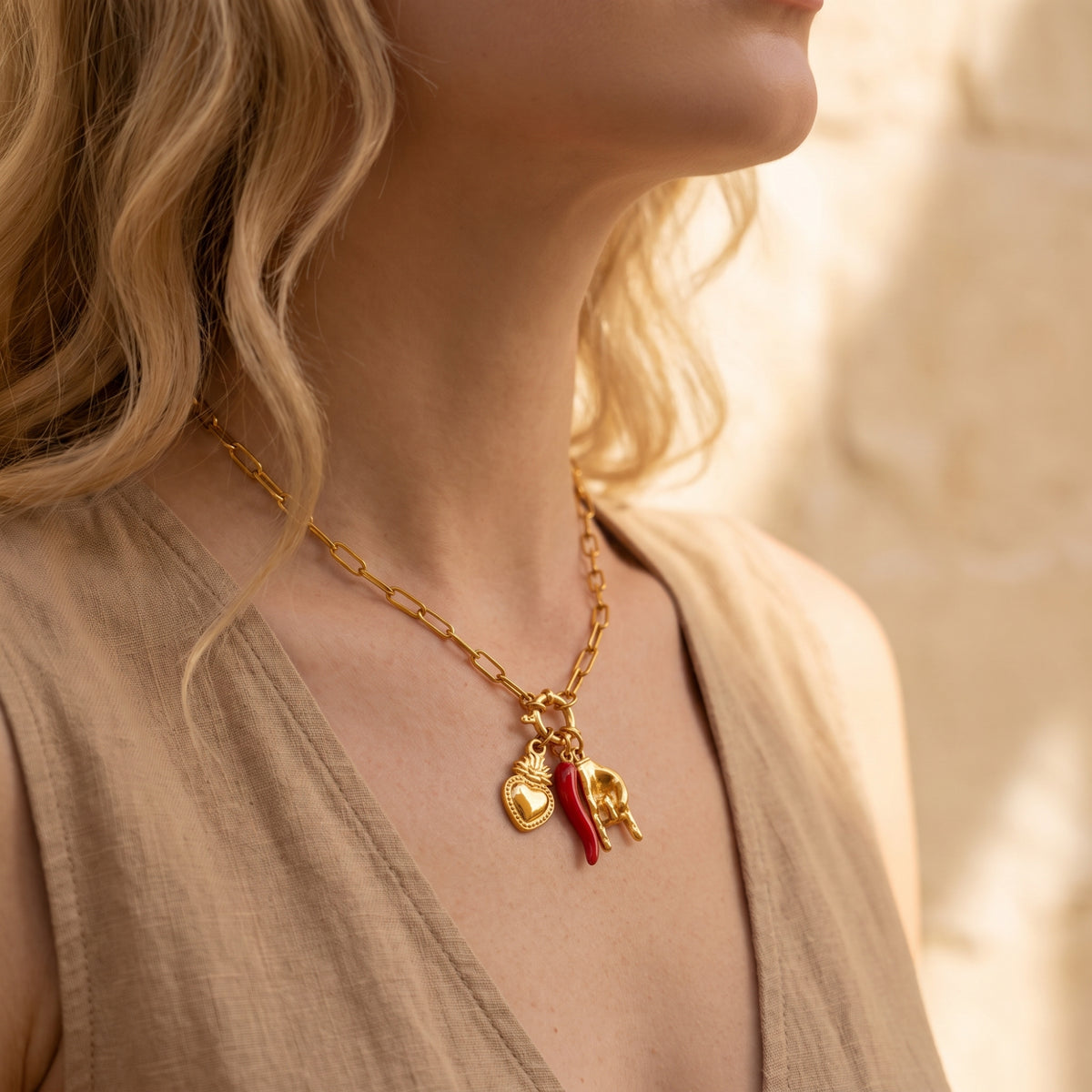Side view of a model wearing the gold-tone paperclip necklace with heart, red pepper, and horned-hand charms.