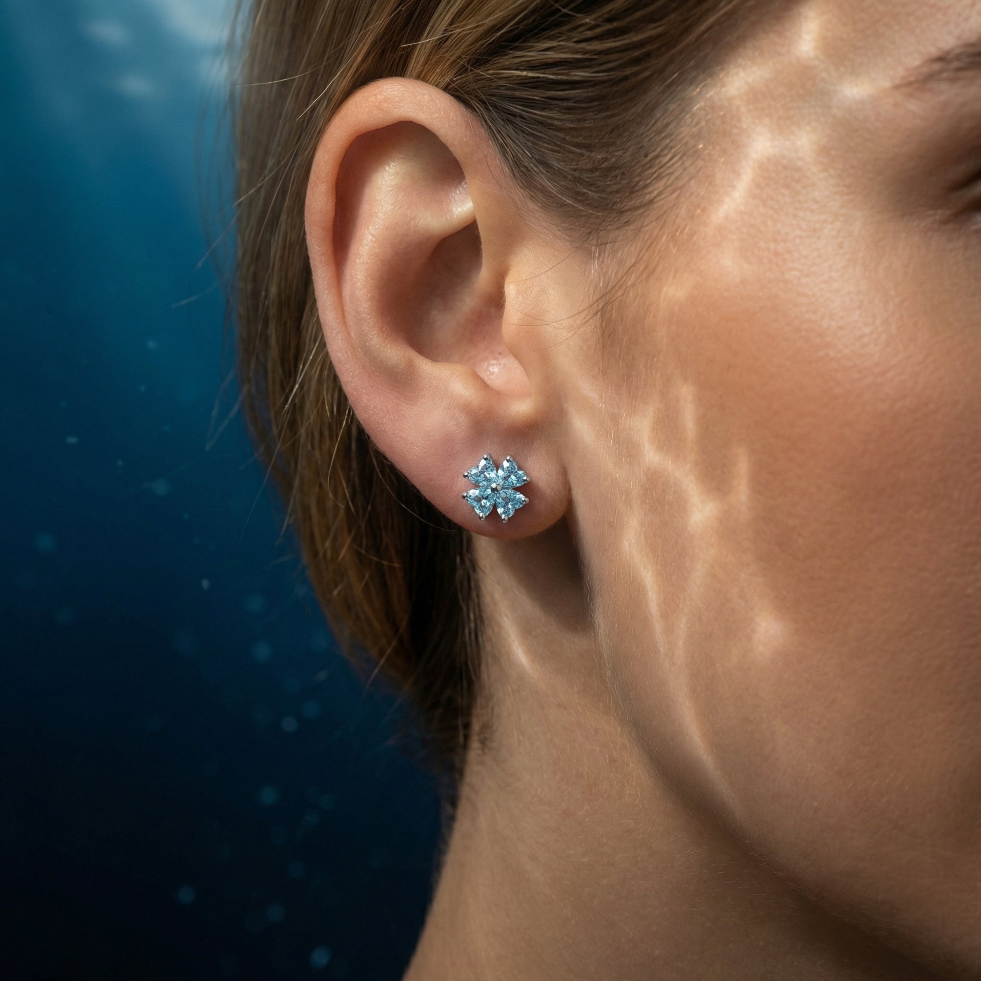 A model wearing the platinum clover stud earring featuring four heart-cut aquamarine stones.