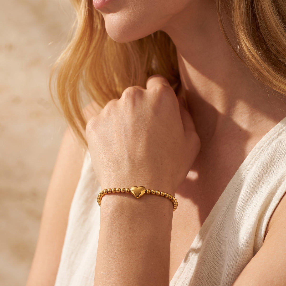 Medium shot of a model wearing the gold-tone beaded heart bracelet, resting her hand near her neck.