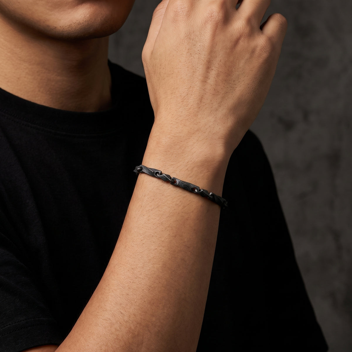 Dark oxidized silver twisted-link bracelet shown from the side on a man's wrist against a black shirt.