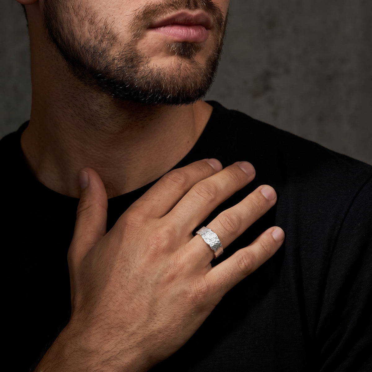 Close-up view of a man resting his hand on his chest, displaying the textured silver band ring.