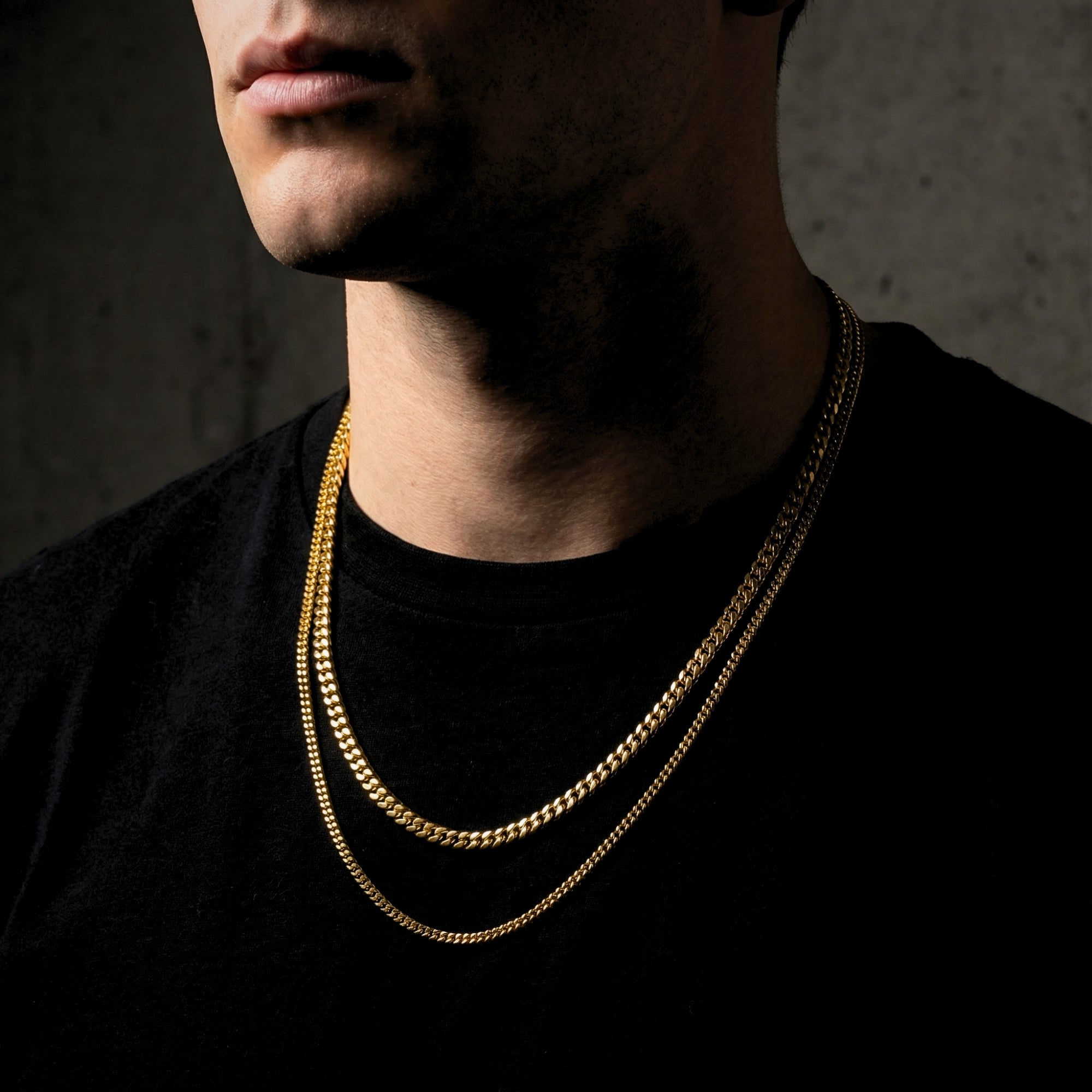 Side view of a man wearing two gold Cuban link necklaces of different lengths.