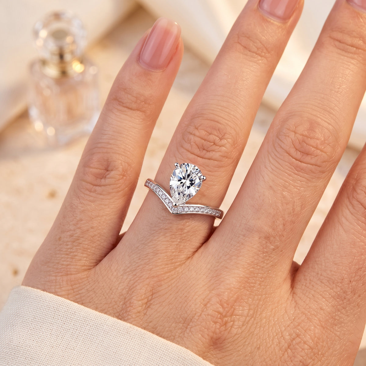 Top-down close-up of a hand wearing a silver V-shaped chevron ring with a pear-shaped center stone and pave accents.