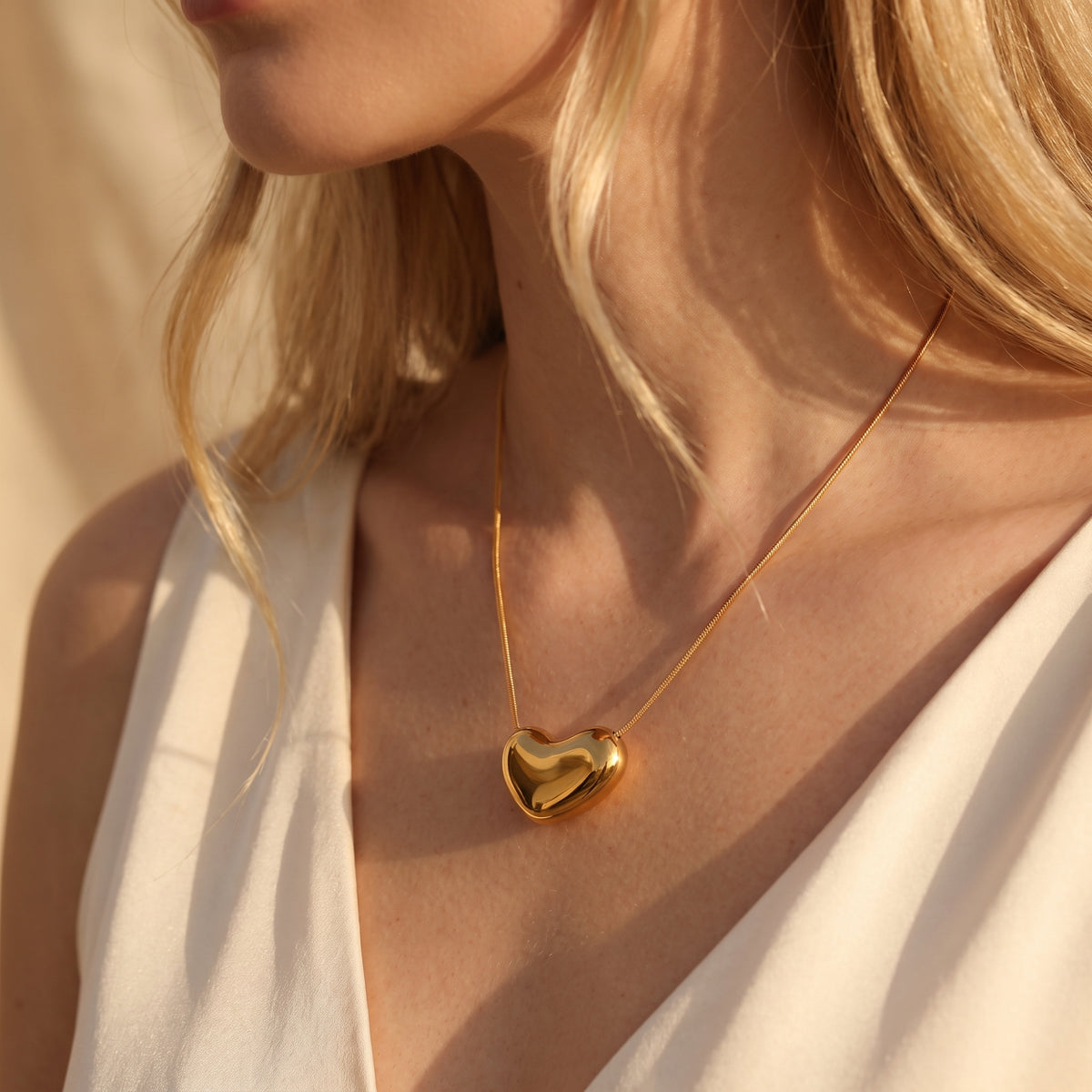 Angled view of a model wearing a gold-tone puffy heart pendant necklace with a V-neck top in sunlight.