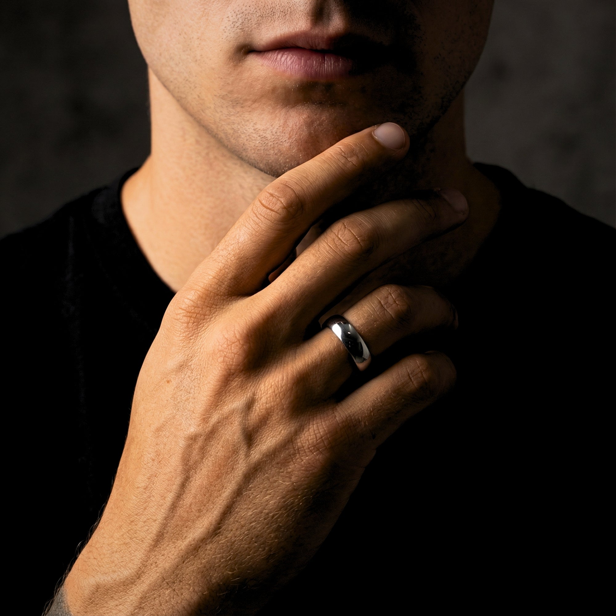 The Minimalist Ring, a silver 5mm stainless steel band for men, worn on a hand touching the chin.