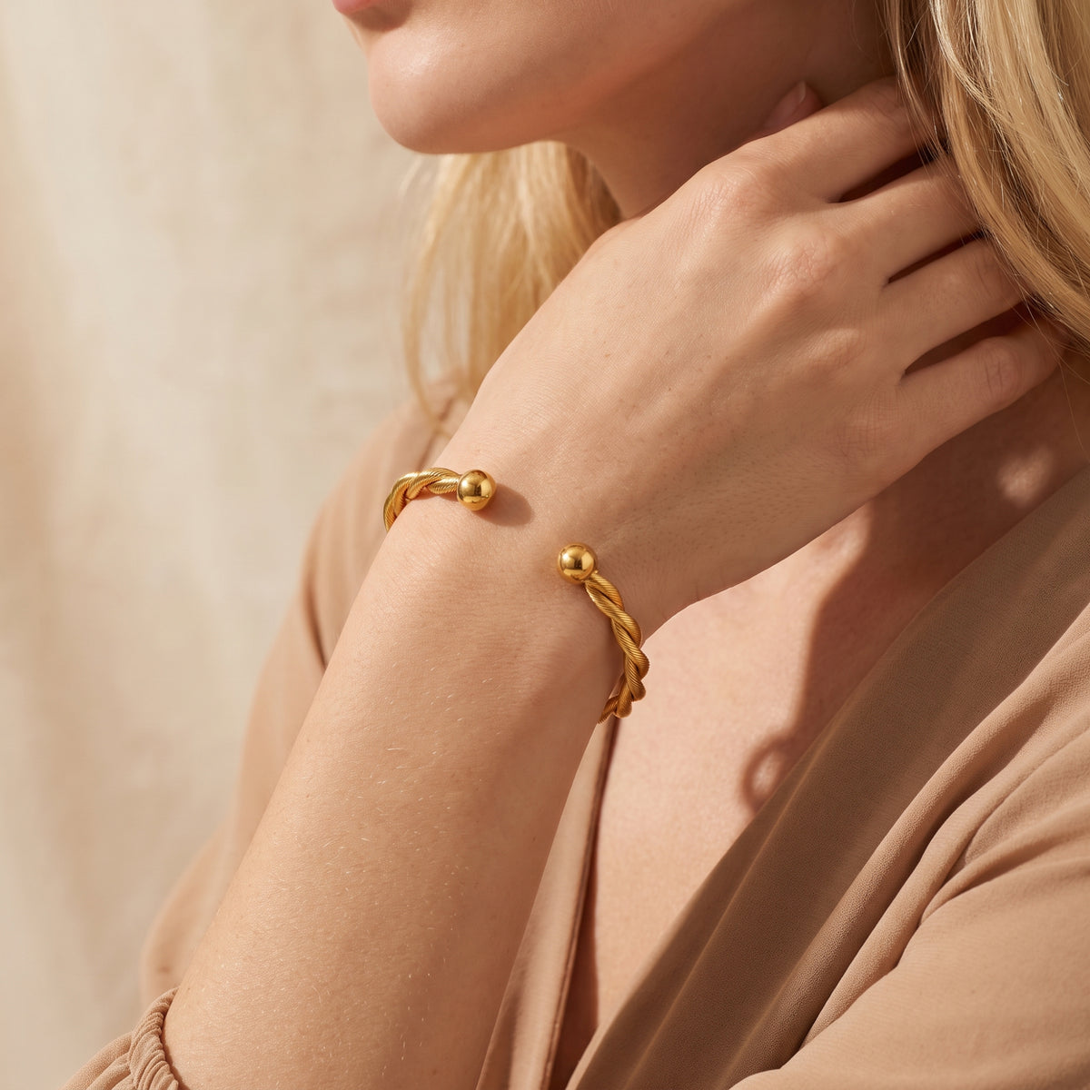 On-model view of the gold-tone twisted cuff bracelet showing the open gap and polished spherical ends.
