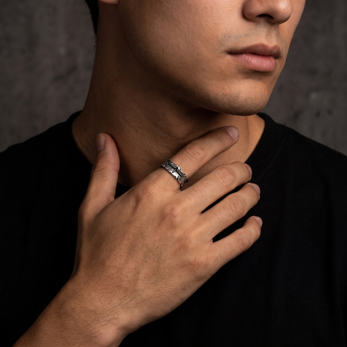 Man wearing the distressed silver cross band ring with his hand resting across his neck.
