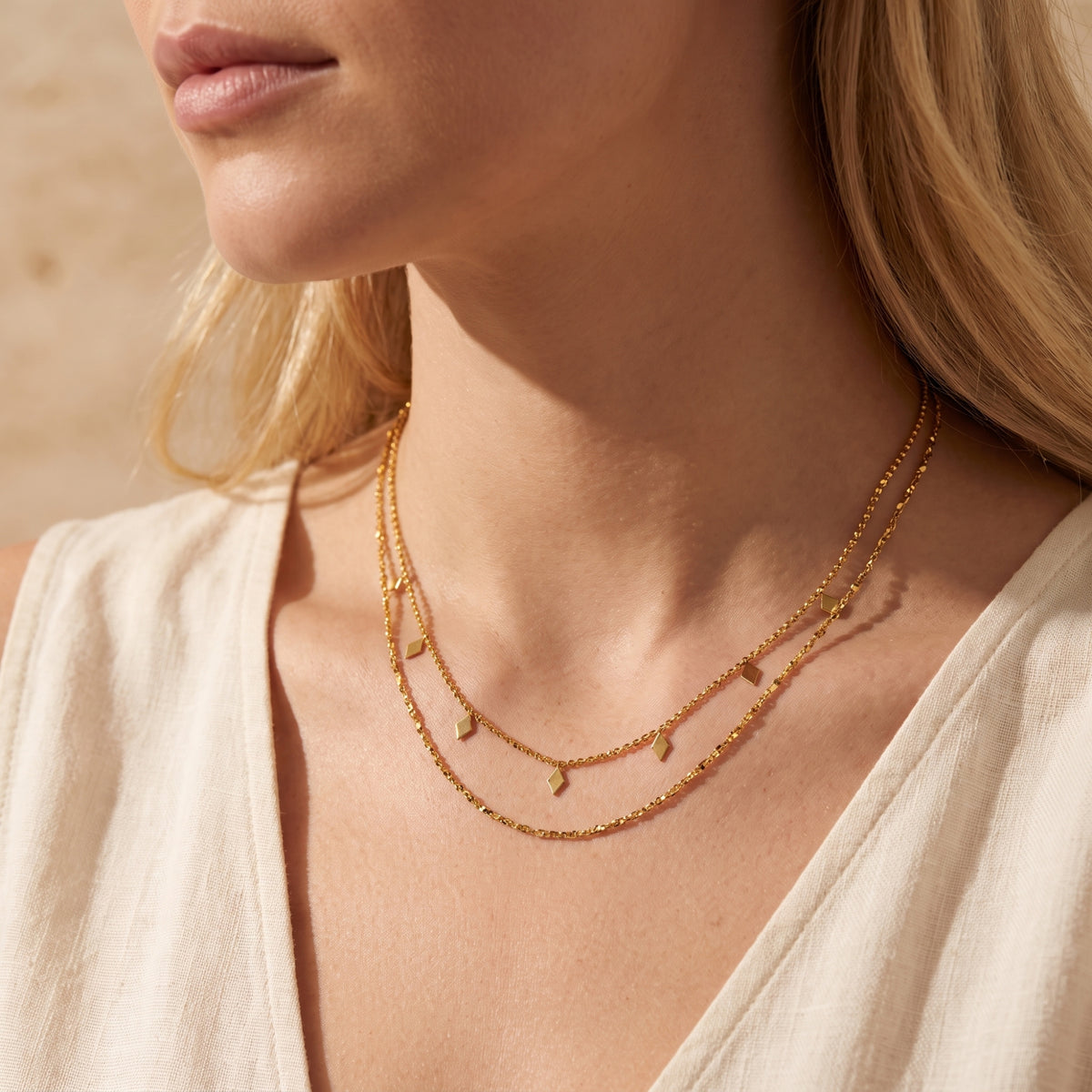 Close-up of a gold-tone layered necklace with diamond-shaped charms worn across a model's collarbone.