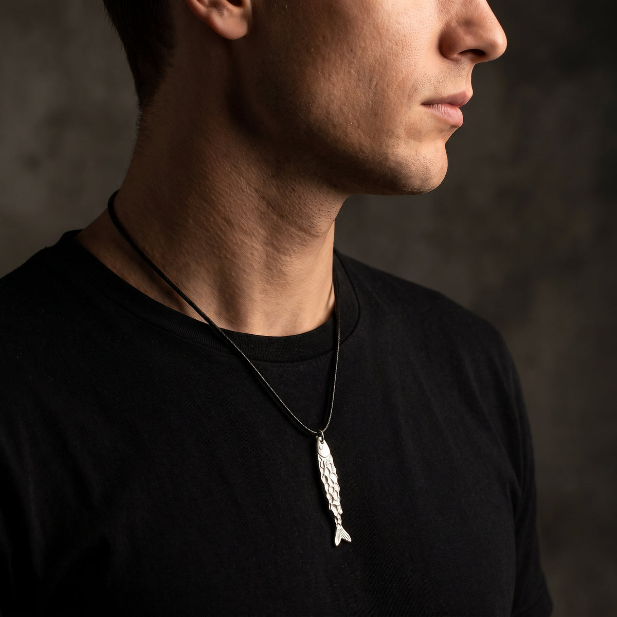 Side profile of a man wearing the silver textured fish pendant necklace on a black cord.