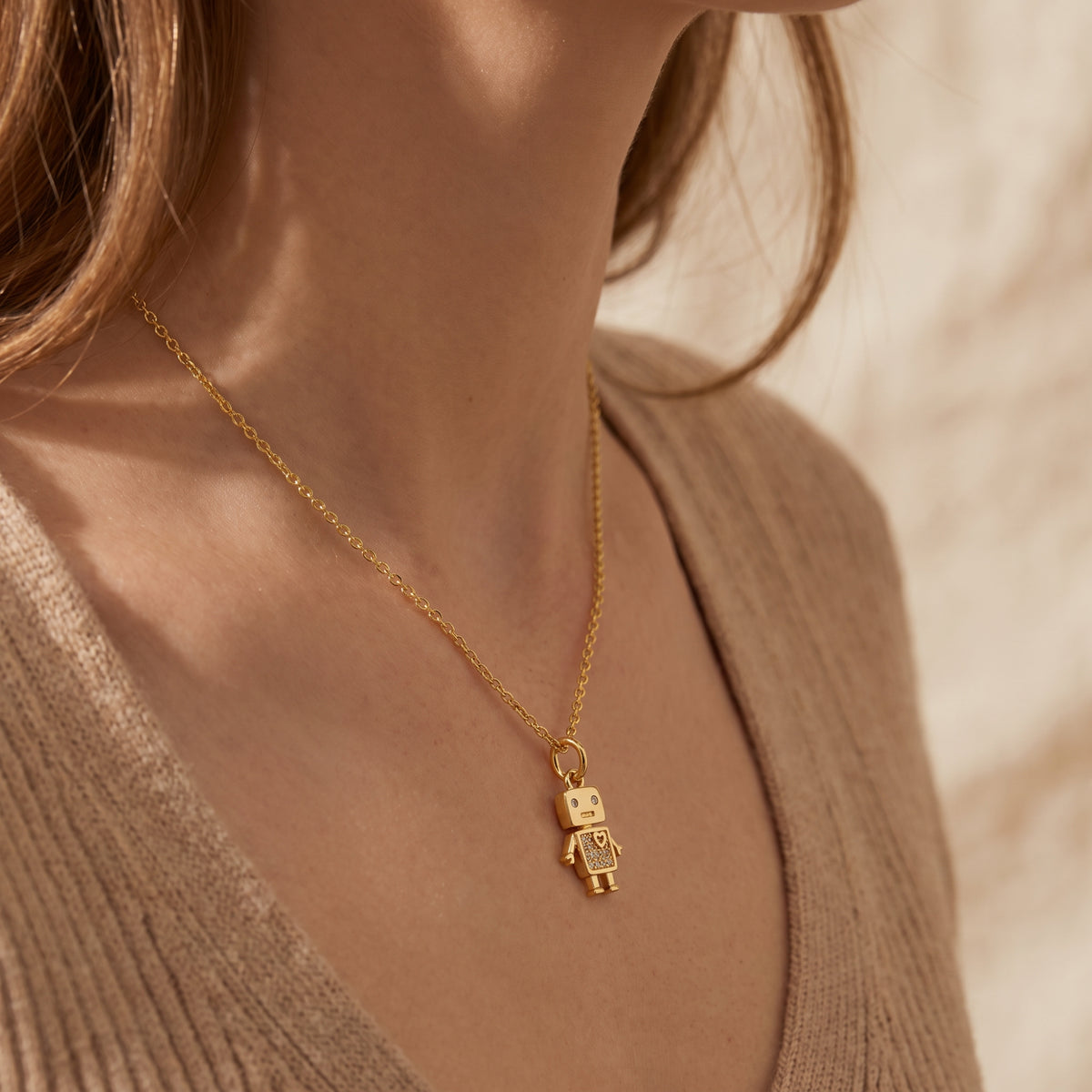 Model wearing a gold-tone robot pendant necklace over a beige ribbed knit top.
