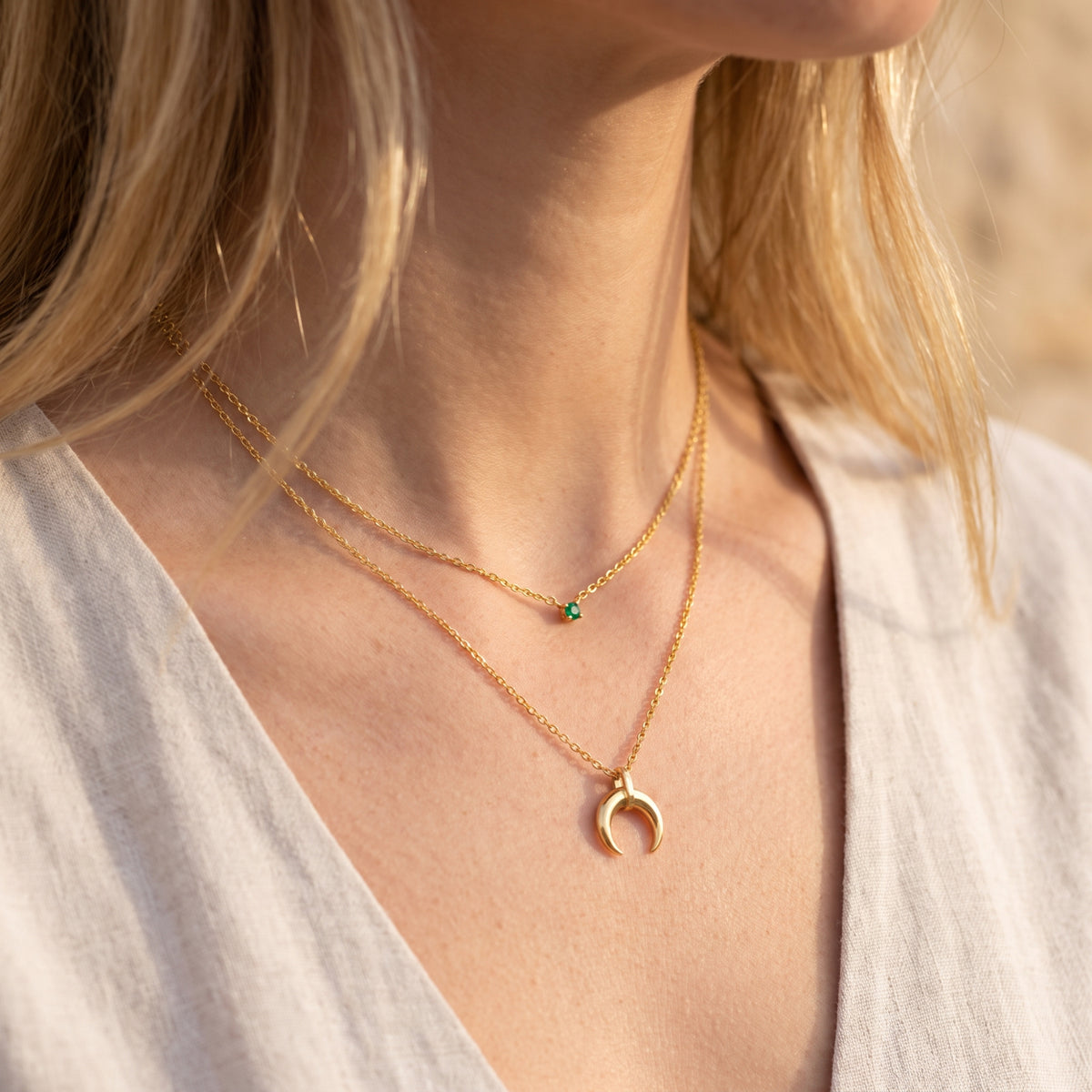 Angled sunlit view of a model wearing the gold-tone layered necklace with green cubic zirconia and crescent pendant.
