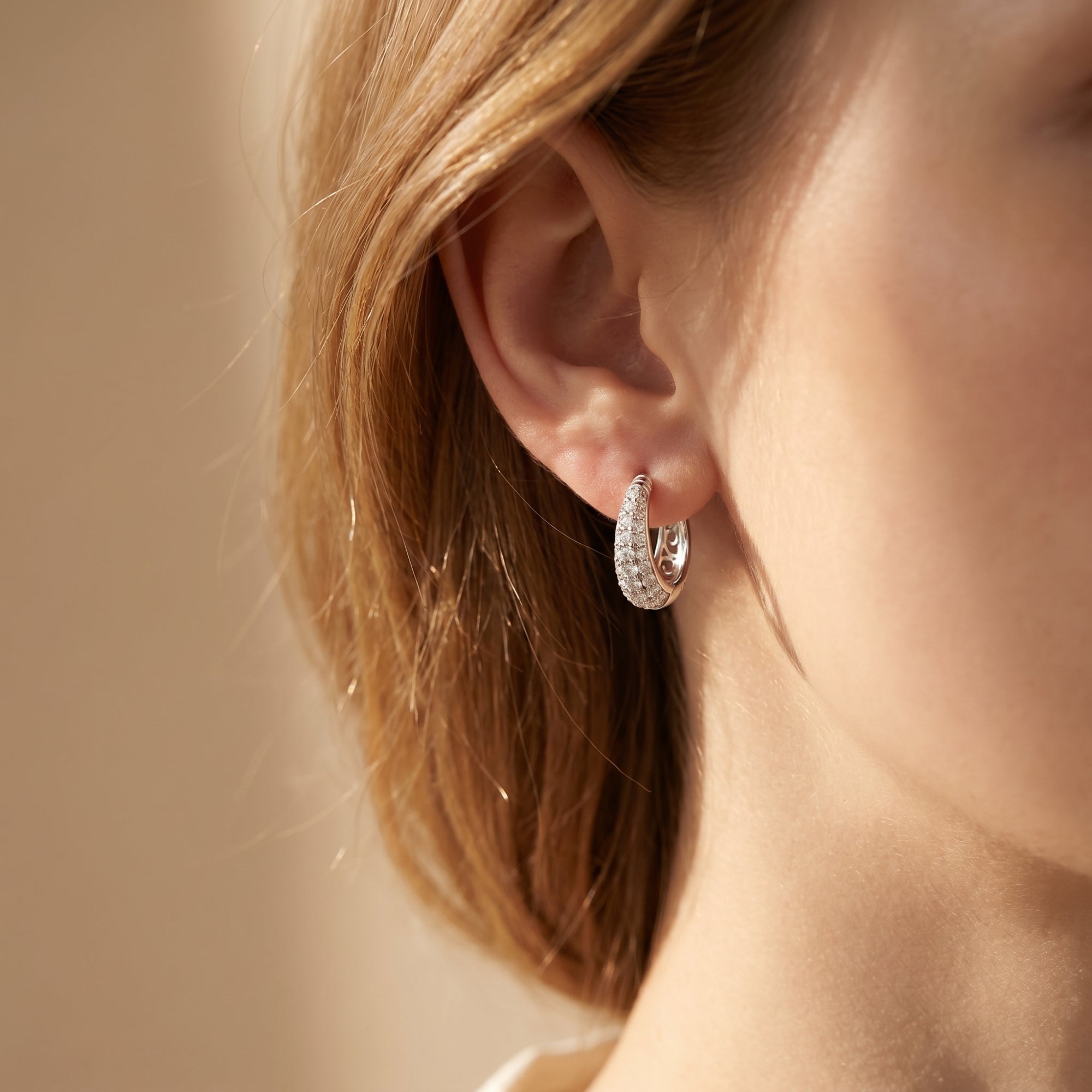 Silver moissanite hoop earrings with brilliant round stones worn on a woman's ear.