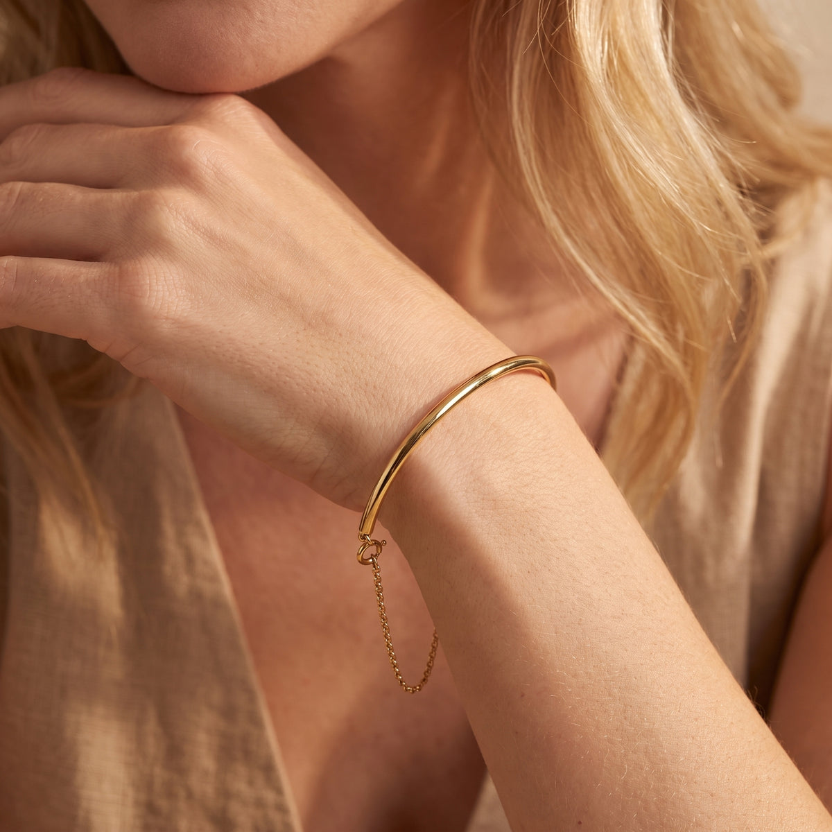 Close-up of a gold-toned arc bracelet worn on a wrist, with its chain hanging below.