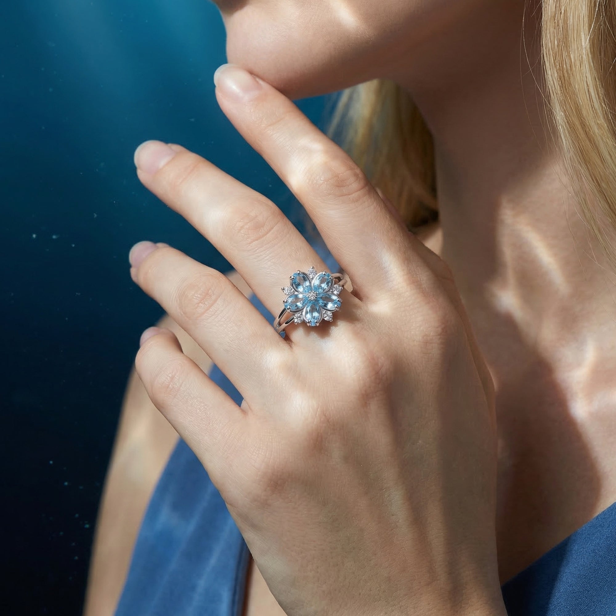 The Undine Blossom aquamarine floral ring in white gold shown on a model's hand against a blue background.